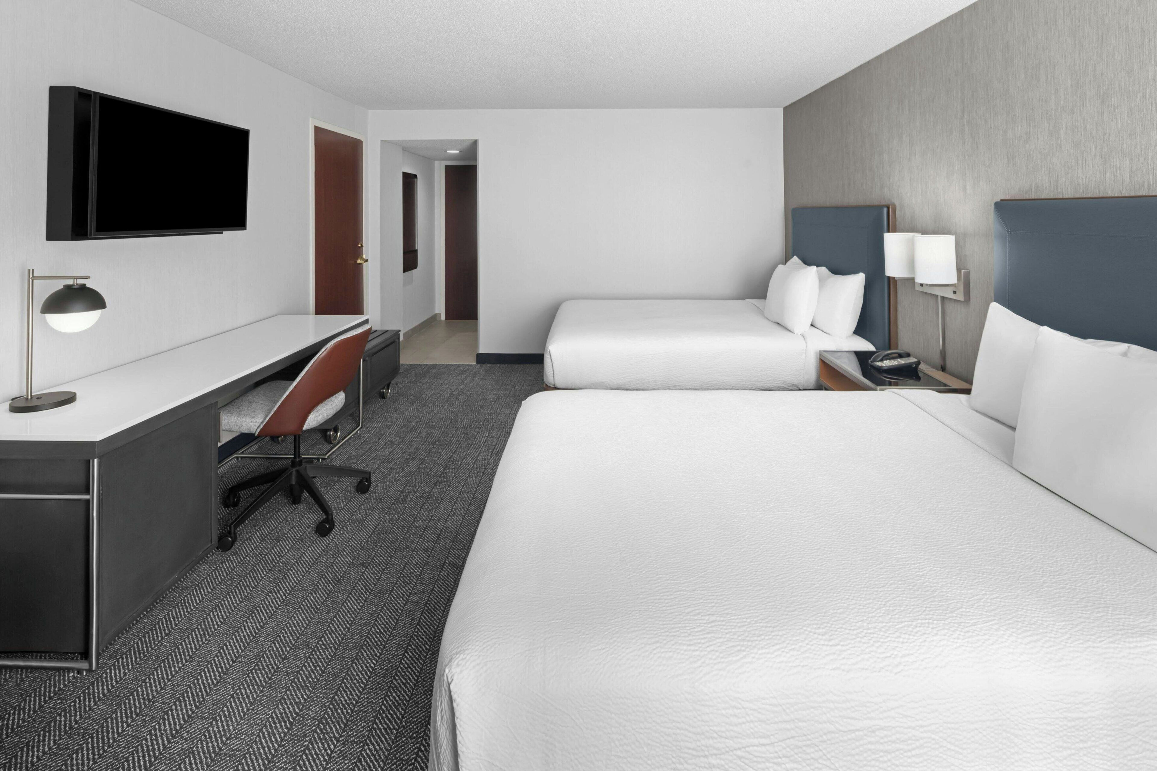 Una habitación de hotel con escritorio, dos camas, televisor y lámpara.