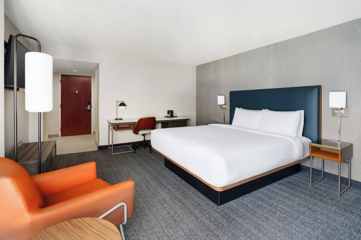 A hotel room with a large bed, a desk, a chair, and a lamp.