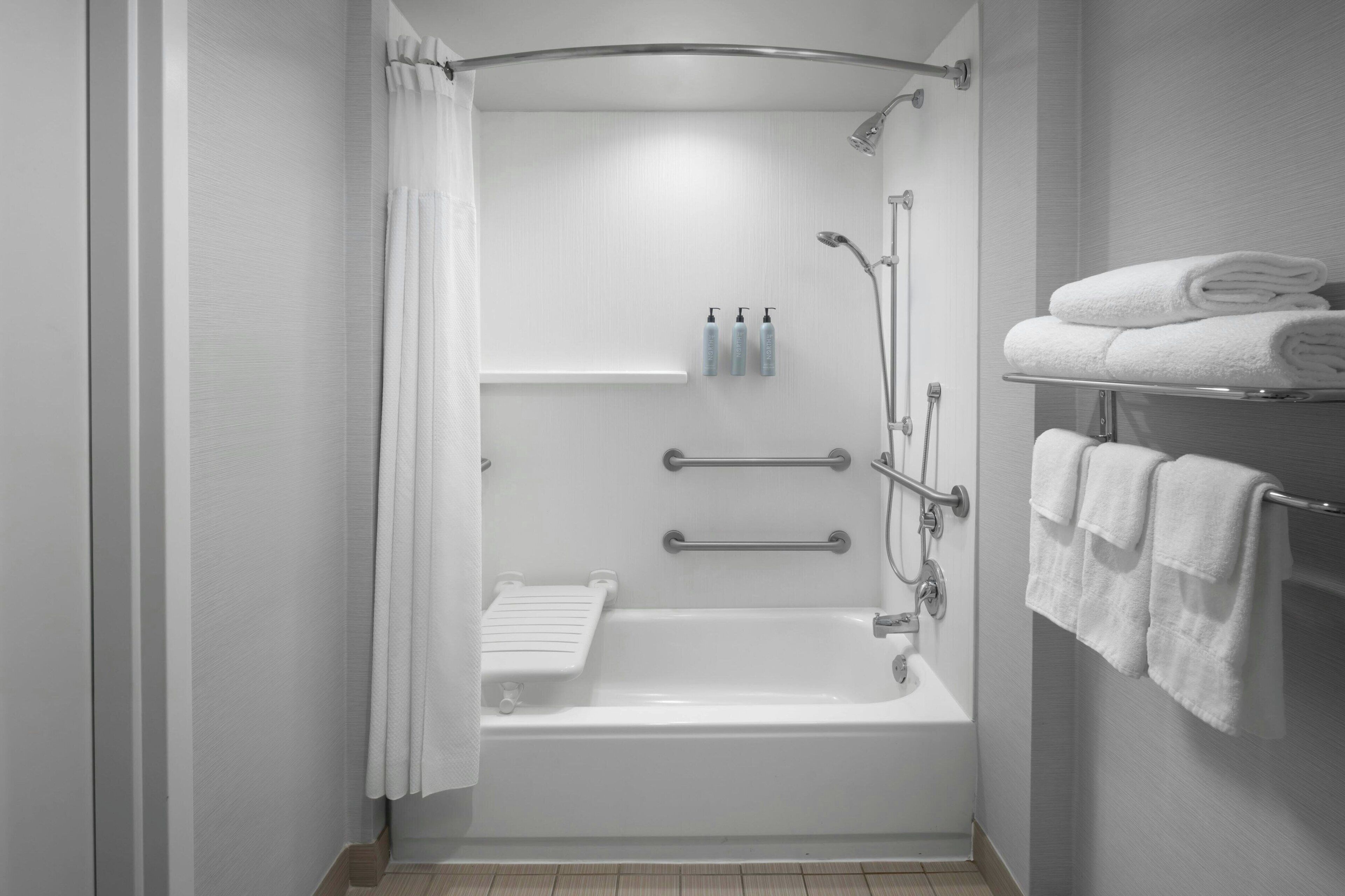 Een moderne badkamer met een inloopdouche, handgrepen, een handdoekrek en een plank met toiletartikelen.