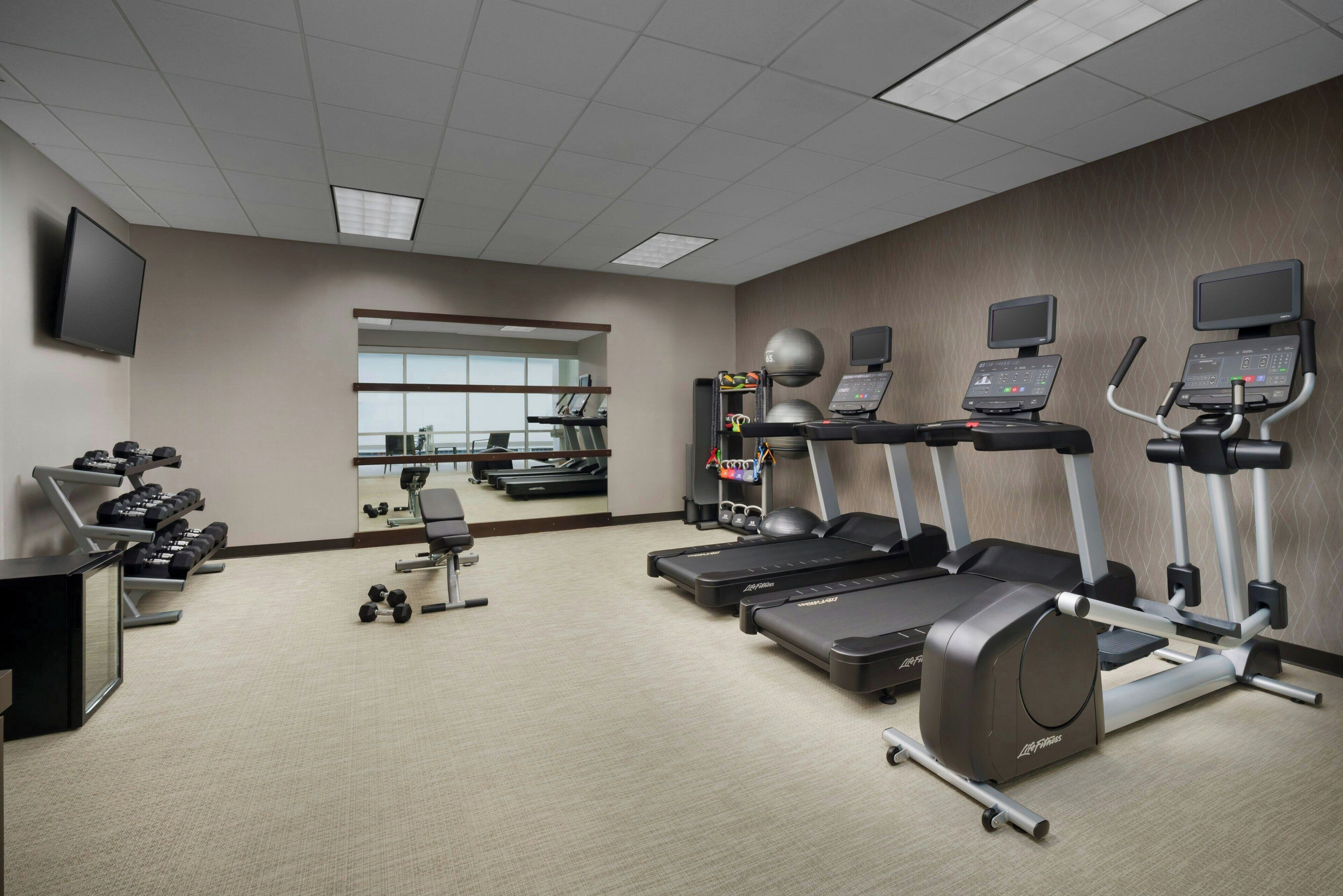 A gym with treadmills, dumbbells, and a mirrored wall.