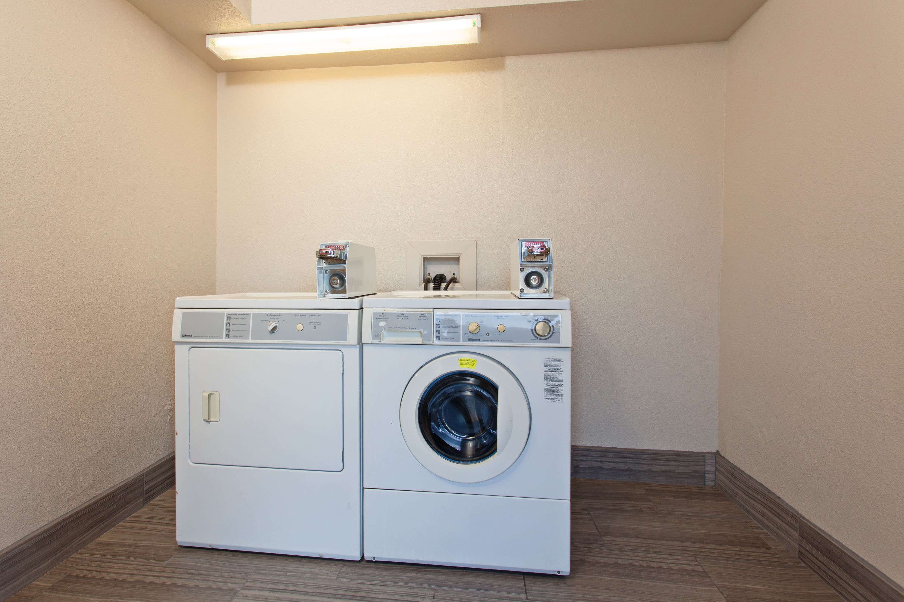A laundry room with two stacked washing machines and dryers, a small shelf with items, and a fluorescent light above.