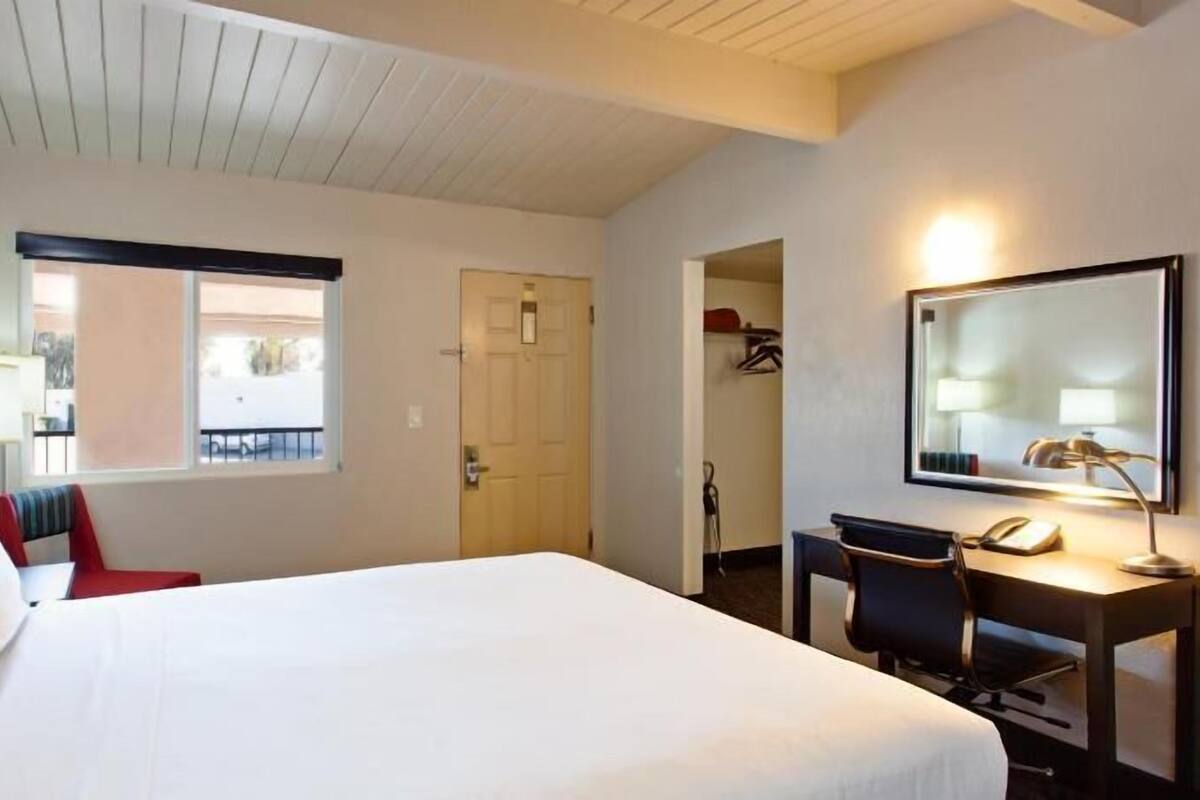 Une chambre d’hôtel avec un lit, un bureau et une chaise, un miroir et une fenêtre.