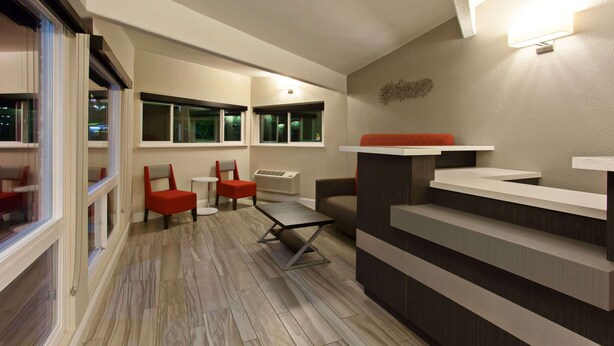 A modern hotel lobby with a wooden floor, seating area with red chairs, a grey sofa, and a reception desk. - Days Inn by Wyndham Chowchilla Gateway to Yosemite (Chowchilla)
