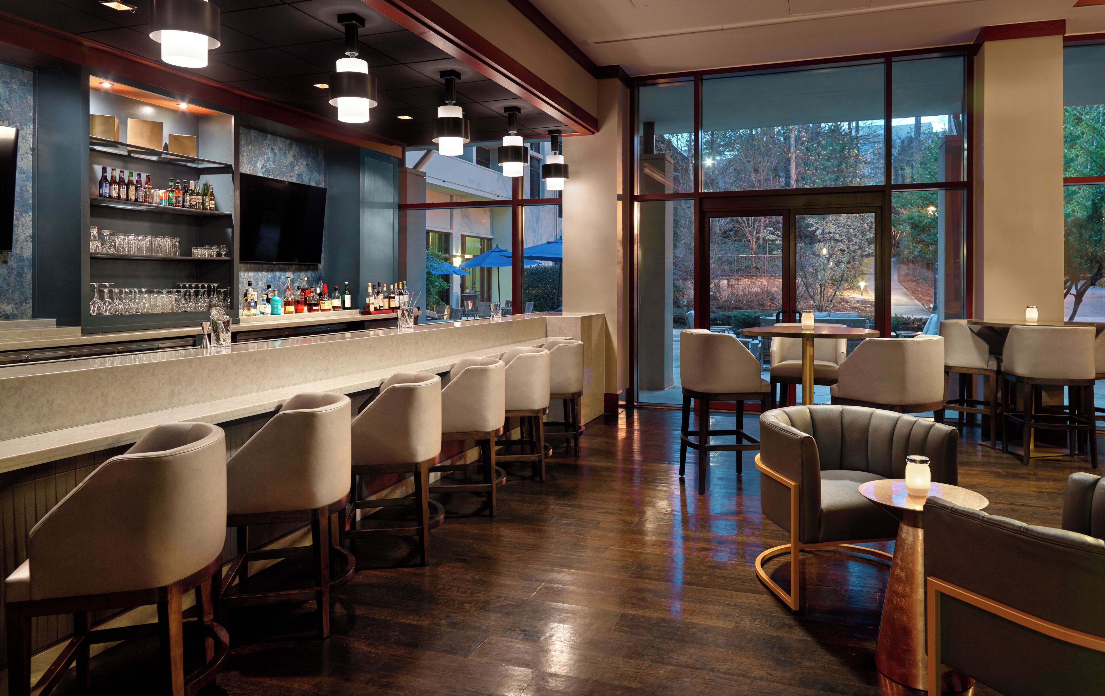 A bar area with a long counter, bar stools, and a view of the outdoors through large windows.