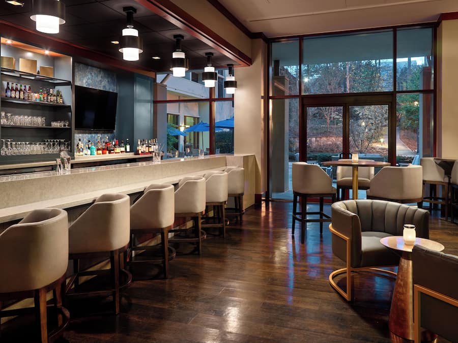 A bar area with a long counter, bar stools, and a view of the outdoors through large windows.