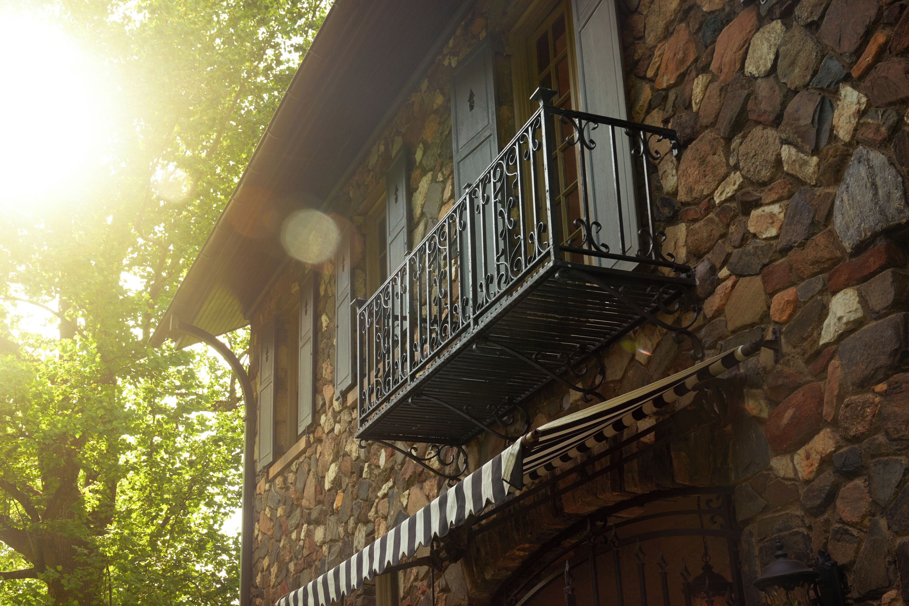 A stone building with a balcony featuring wrought iron railings and a striped awning.