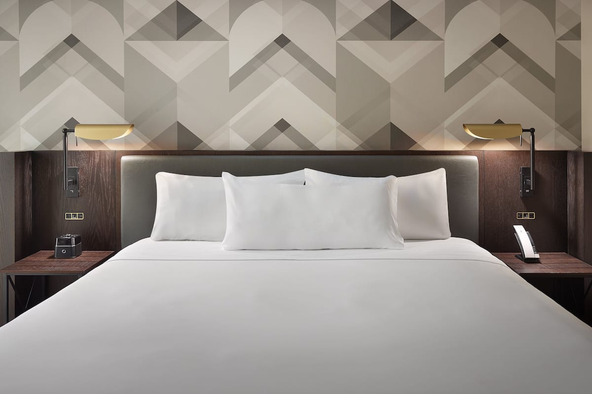 A neatly made bed with white linens, two bedside tables with lamps, and a geometric patterned wall.