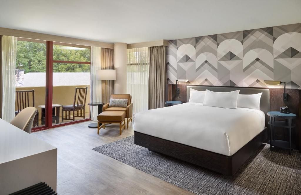 A hotel room with a large bed, a desk, a chair, and a view of the outdoors.