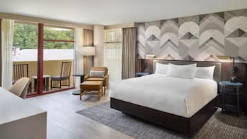 A hotel room with a large bed, a desk, a chair, and a view of the outdoors.