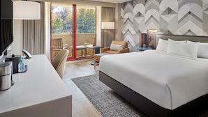 A hotel room with a bed, a desk, a chair, a small table, and a view of the outdoors through a sliding door. - Emory Conference Center Hotel (Atlanta)