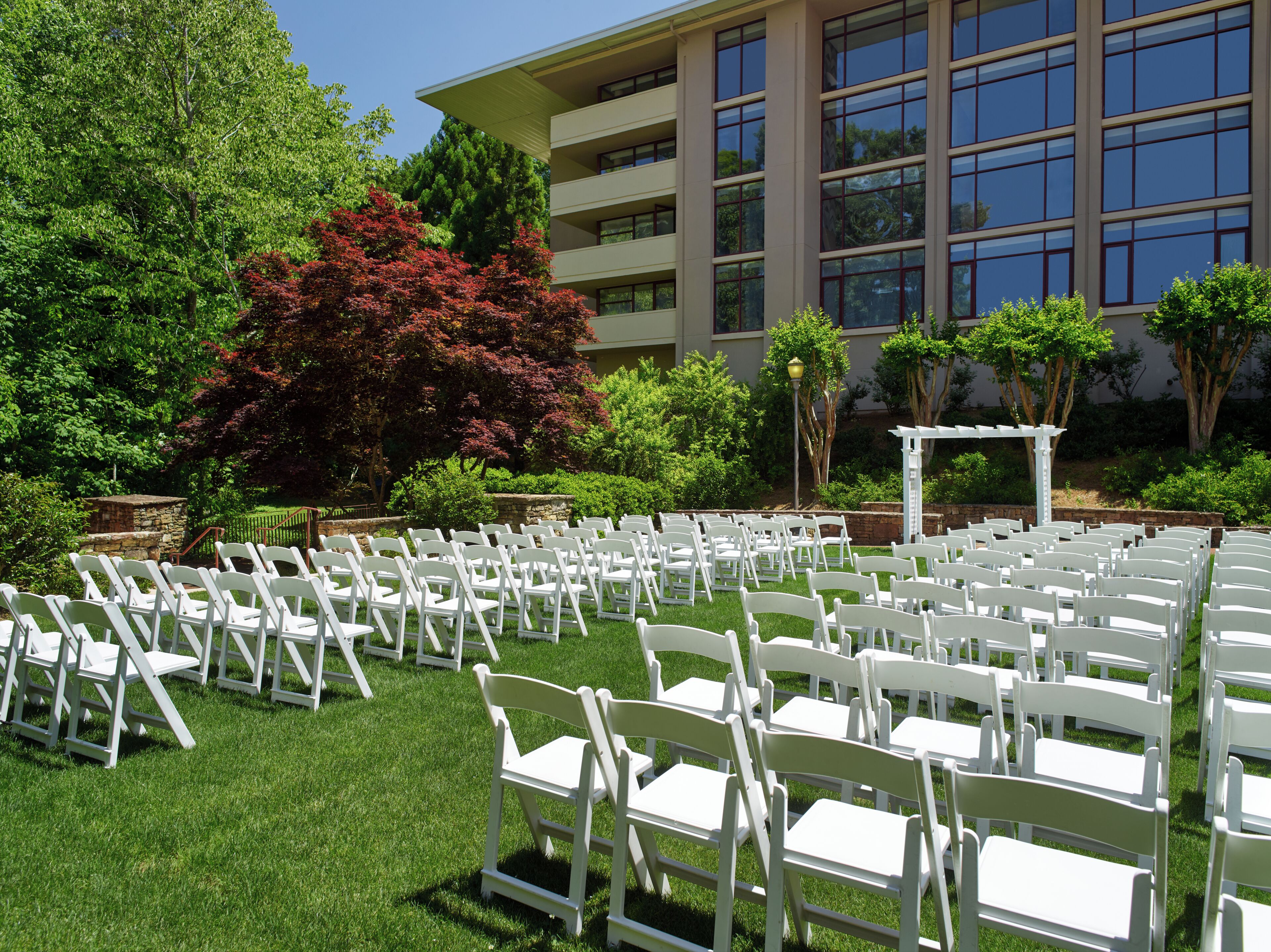 A lawn with white chairs arranged in rows, a stone structure, and a building with large windows in the background.