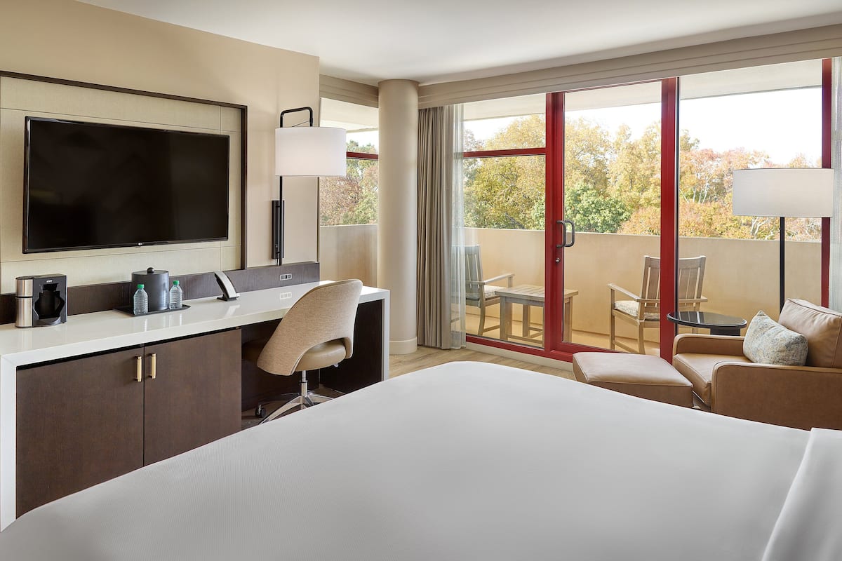 A hotel room with a bed, a desk with a TV, a coffee maker, and a view of the outdoors.