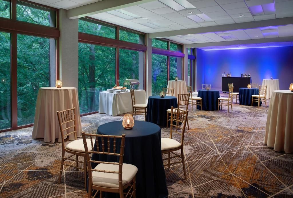 Een vergaderzaal met ronde tafels, stoelen en een podium met een blauwe achtergrond.