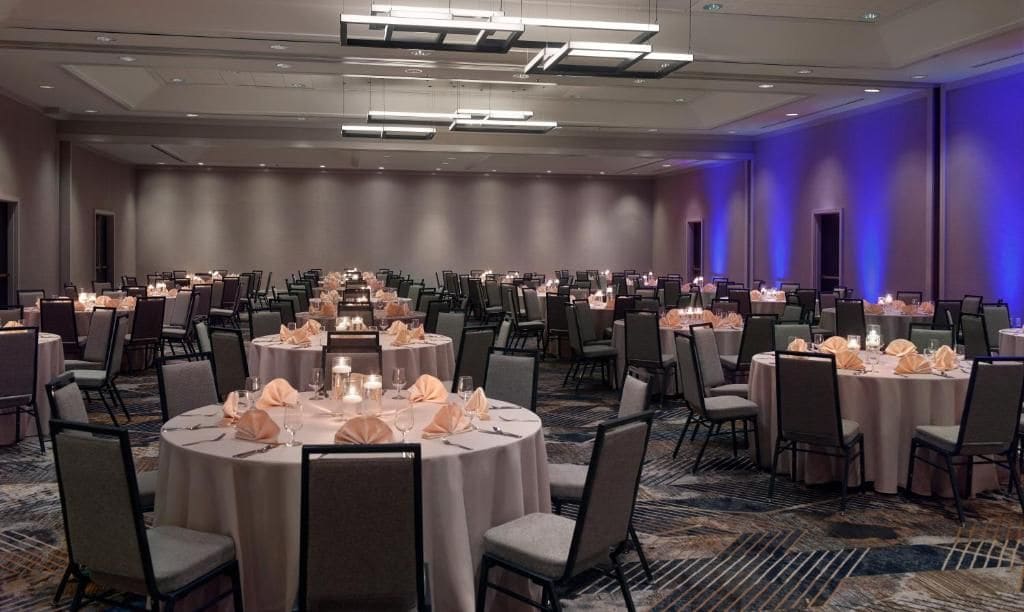 Un salón de banquetes con varias mesas redondas, cada una dispuesta con sillas, centros de mesa y mantelería.