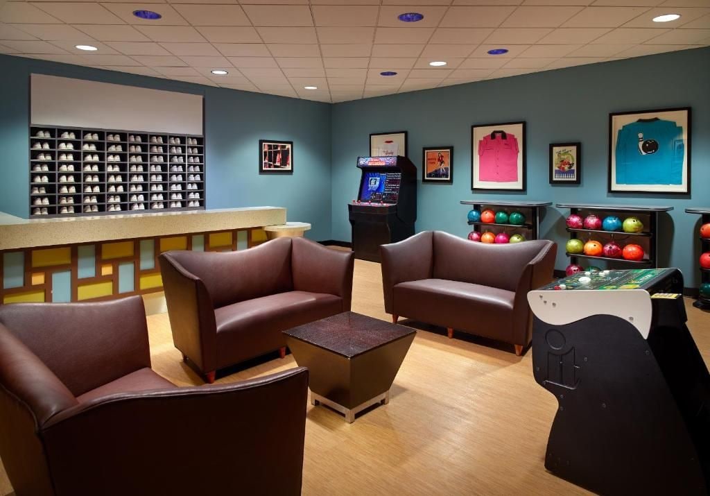 Une salle de bowling avec des sièges, un présentoir à boules et un appareil pour remettre les quilles en place.