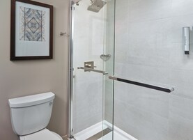 Un baño moderno con cabina de ducha de vidrio, un inodoro y una obra de arte enmarcada en la pared.