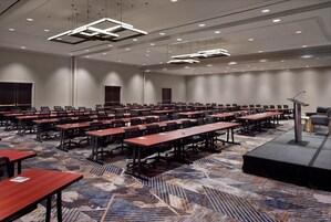 A conference room with multiple tables and chairs, a stage with a podium, and a carpeted floor.