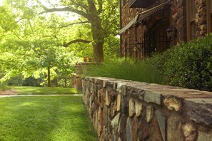 A stone wall with a grassy lawn and a large tree.