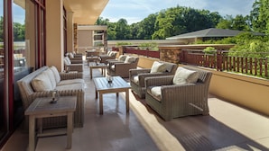 A covered outdoor seating area with wicker furniture and tables, a stone wall, and a view of the surrounding greenery. - Emory Conference Center Hotel (Atlanta)