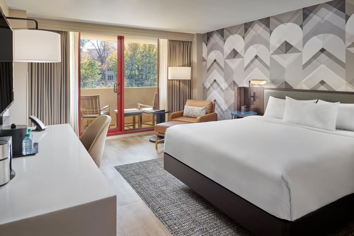 A hotel room with a large bed, a desk, a chair, a table, and a view of the outdoors.