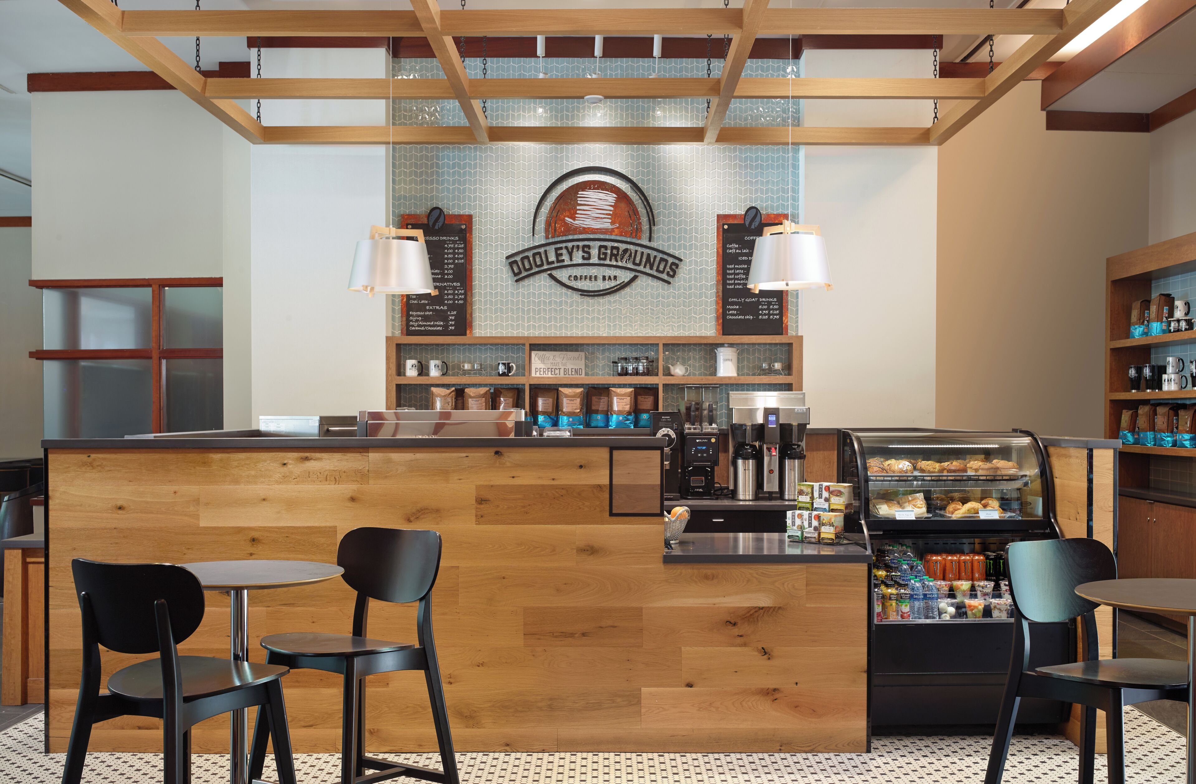 Interior d'una cafeteria amb un taulell de fusta, dues làmpades penjants, una màquina de cafè i una vitrina amb pastissos.