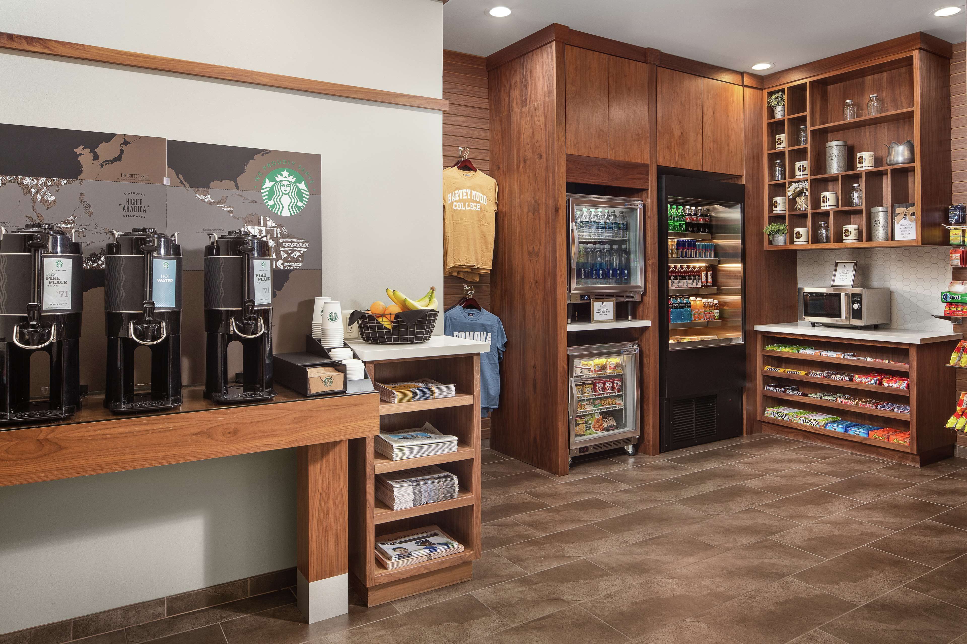 Una cafetería con varias máquinas de café, un refrigerador lleno de bebidas y estantes con aperitivos y aderezos.