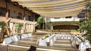 An outdoor wedding venue with white tables and chairs, a stone fireplace, and a covered seating area. - DoubleTree by Hilton Claremont (Claremont)