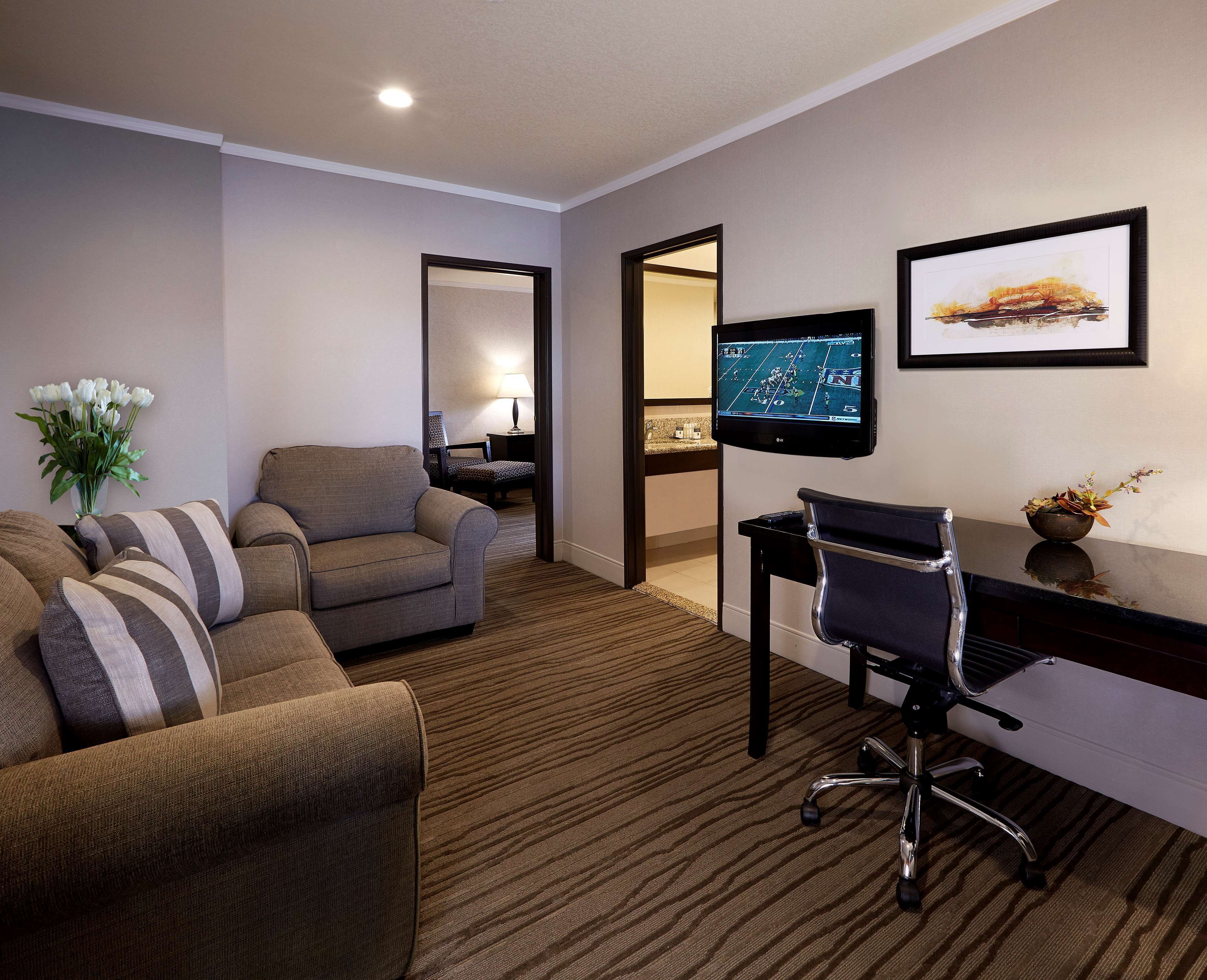 A hotel room with a sofa, a desk with a chair, a television, and a framed picture on the wall.