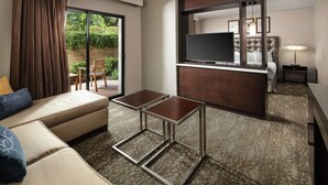 A hotel room with a sofa, two tables, a TV, a bed, and a view of greenery outside. - DoubleTree by Hilton Claremont (Claremont)