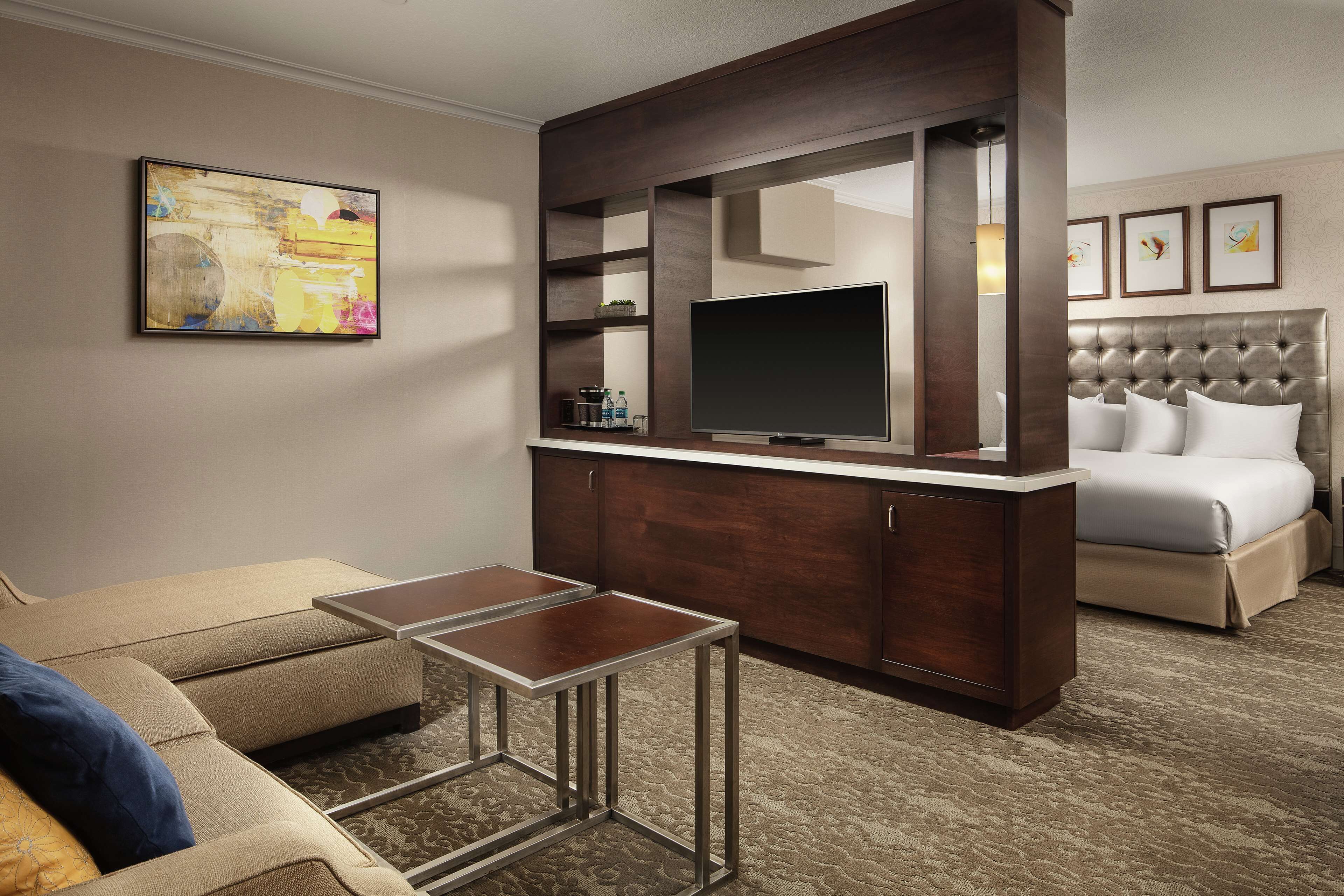 A hotel room with a large bed, a TV mounted on a wooden cabinet, a small table, and a sofa.