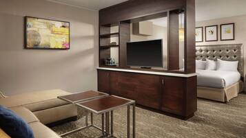 A hotel room with a large bed, a TV mounted on a wooden cabinet, a small table, and a sofa.