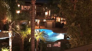 A nighttime view of a hotel with a swimming pool surrounded by palm trees and a lit-up building. - DoubleTree by Hilton Claremont (Claremont)