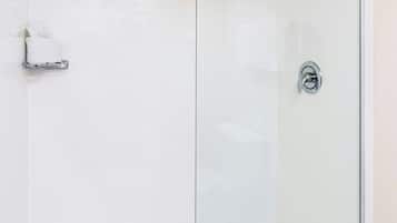 A glass-enclosed shower with a chrome showerhead and a control knob.