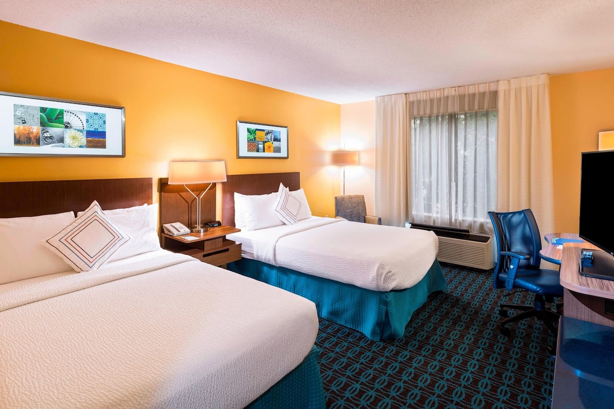 A hotel room with two beds, a desk, a chair, a TV, and a window with curtains.