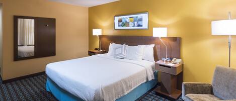 A hotel room with a large bed, two bedside tables with lamps, a chair, a mirror, and a framed picture on the wall.