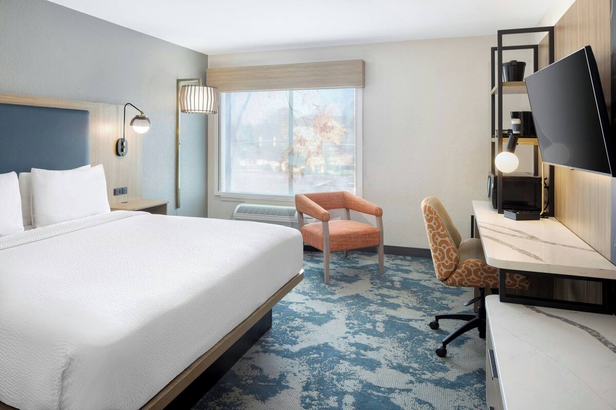 Een hotelkamer met een bed, een bureau, een stoel, een televisie en een raam met uitzicht.