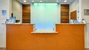 Un mostrador de recepción con acabado de madera, una cortina azul y carteles informativos en la pared.