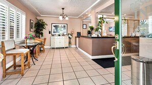 A hotel lobby with a reception desk, a dining area with chairs and a table, and a tiled floor. - Carmel Resort Inn (Carmel)