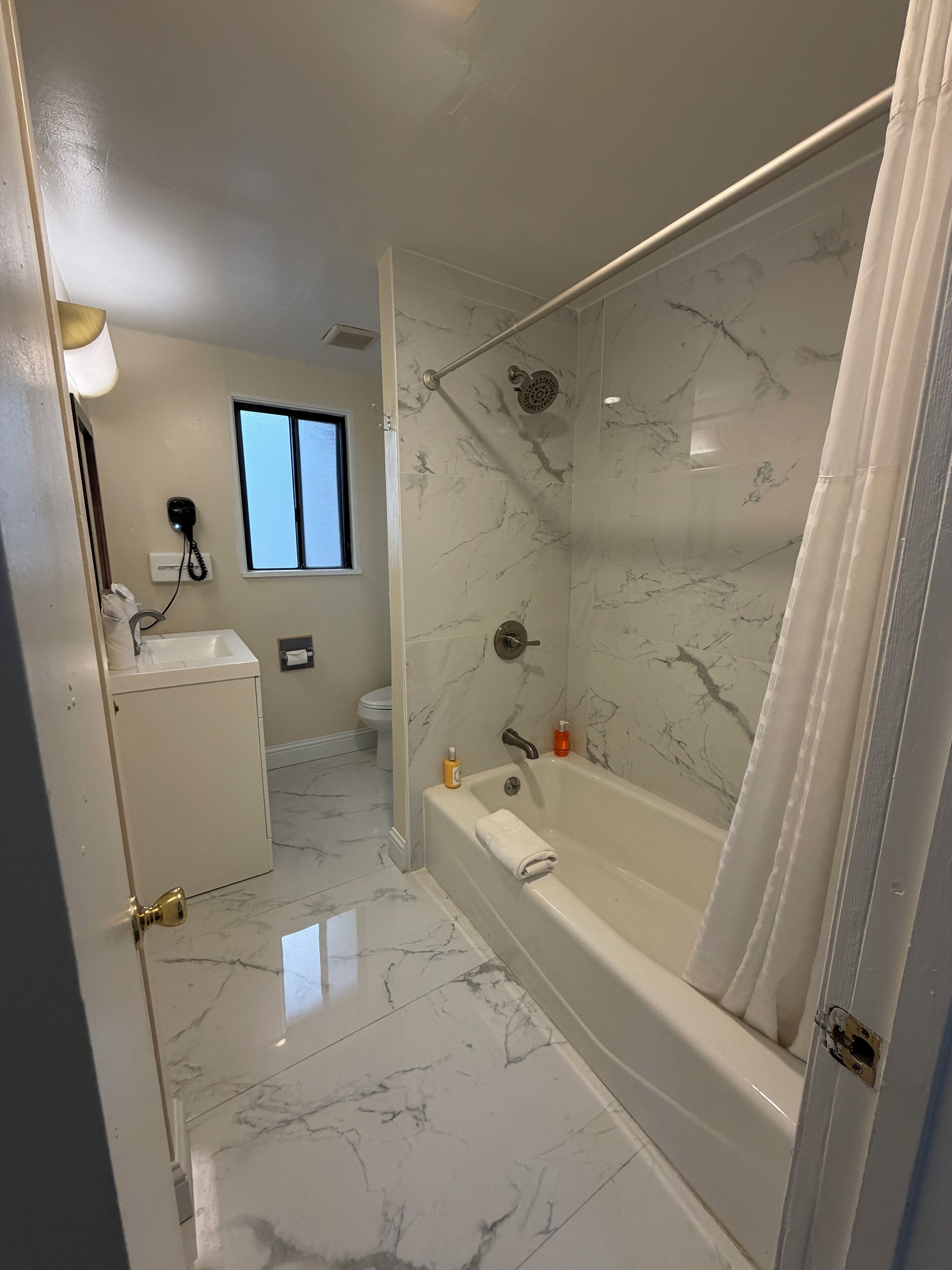 A bathroom with a marble floor, a bathtub, a shower, a toilet, and a sink.