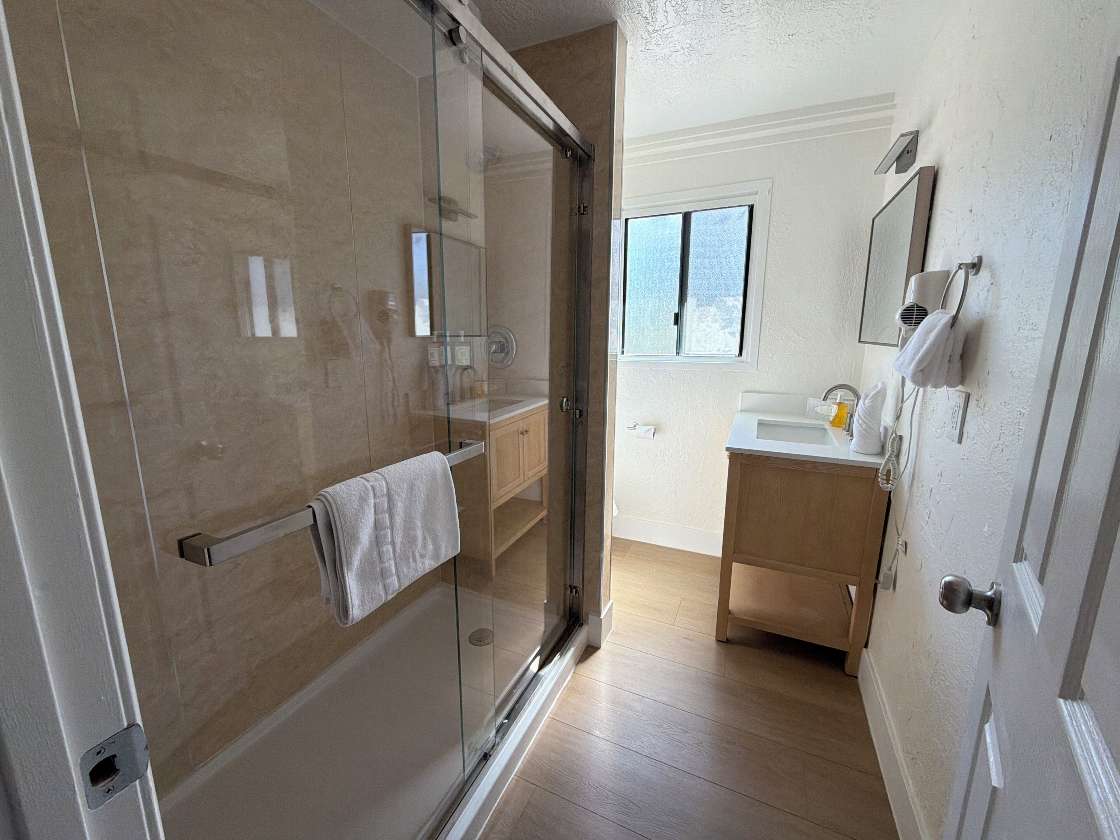 Ein Badezimmer mit Duschkabine aus Glas, einem Holzbadezimmermöbel und einem Fenster für natürliches Licht.