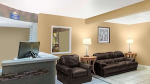 A hotel lobby with a reception desk, two leather sofas, two lamps, a framed picture, and a mirror.