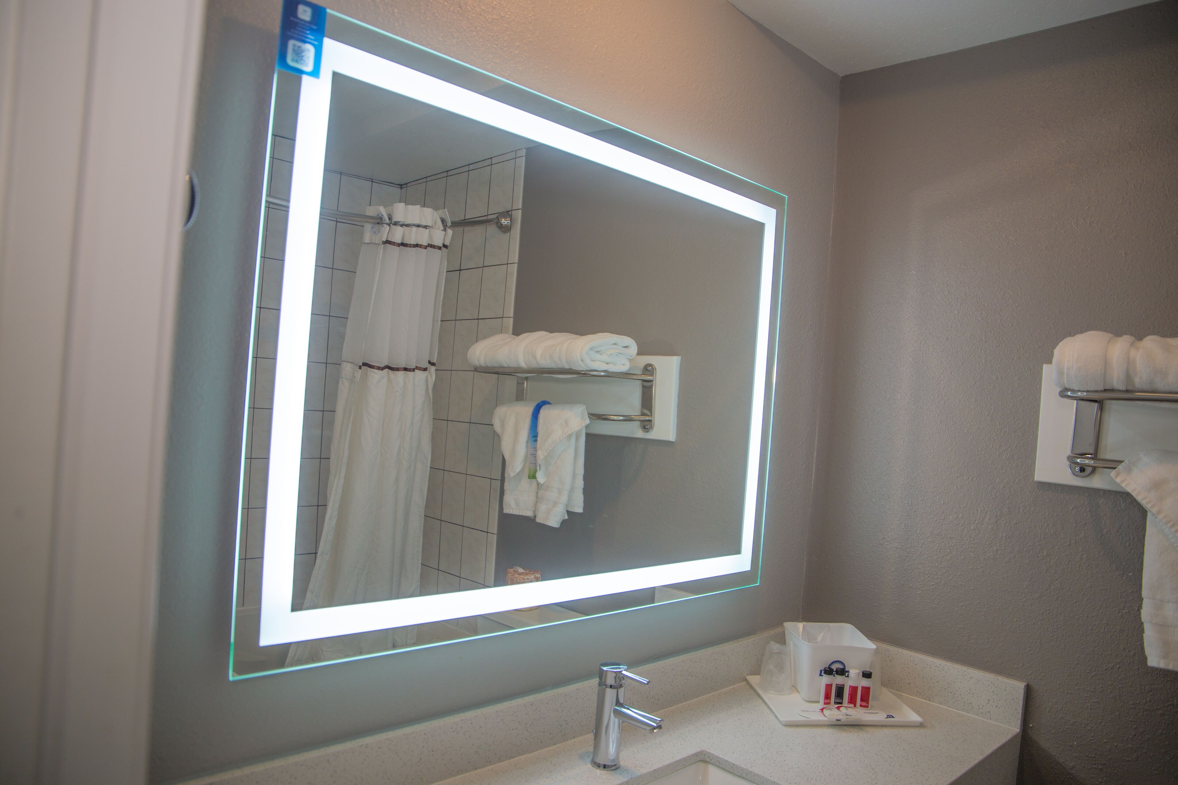 A bathroom with a large mirror, a sink, and a towel rack.