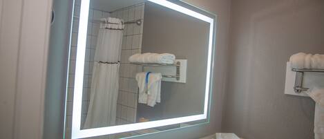 A bathroom with a large mirror, a sink, and a towel rack.