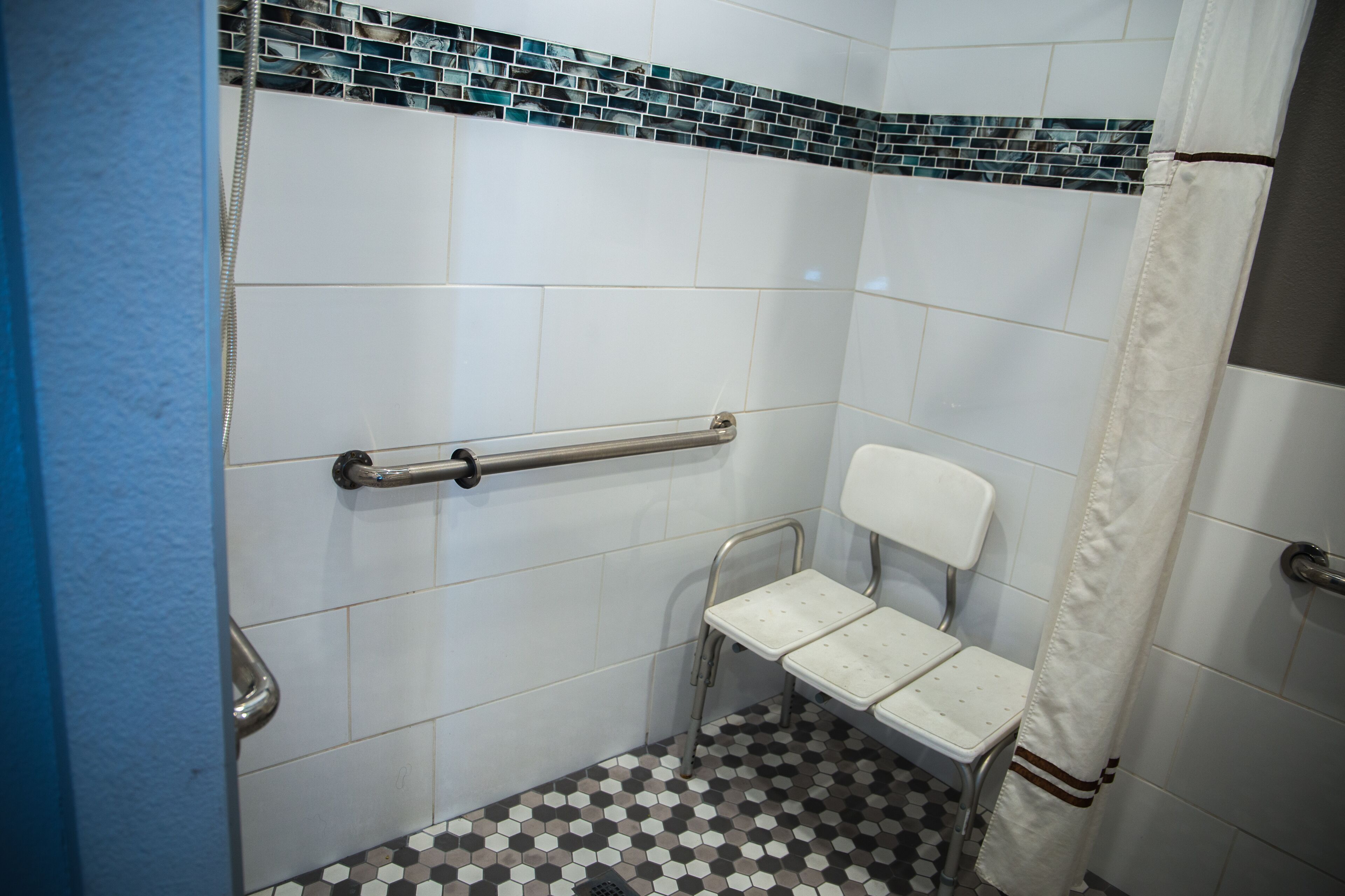 Ein kleines Badezimmer mit gefliesten Wänden, einer weißen Toilette, einer Haltestange und einer Duschvorhang.