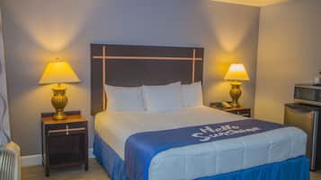 Habitación de hotel con una cama, dos lámparas de noche, una mesita pequeña, un microondas y un refrigerador.