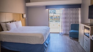 A hotel room with a bed, a desk with a TV, a chair, and a view of the outside.