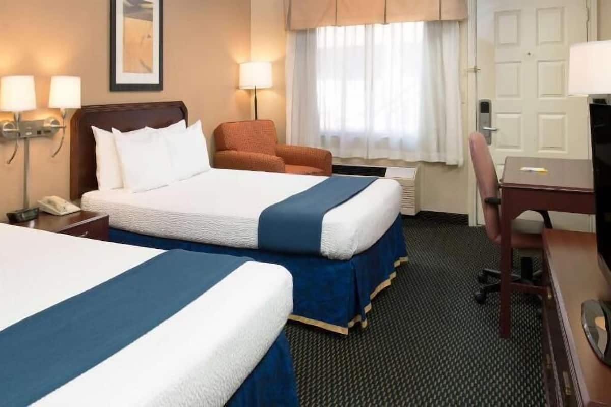 A hotel room with two beds, a desk, a chair, and a window with curtains.
