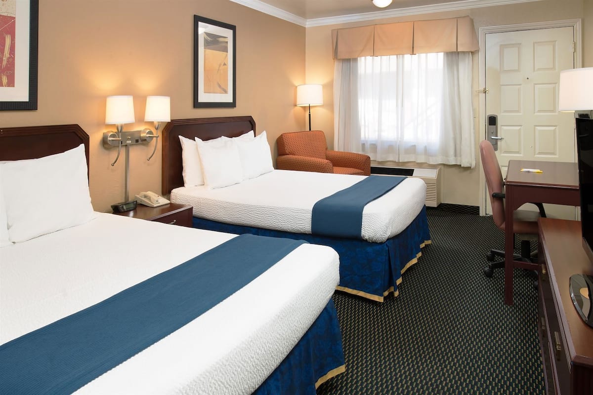 A hotel room with two beds, a desk, a chair, a telephone, and a window with curtains.