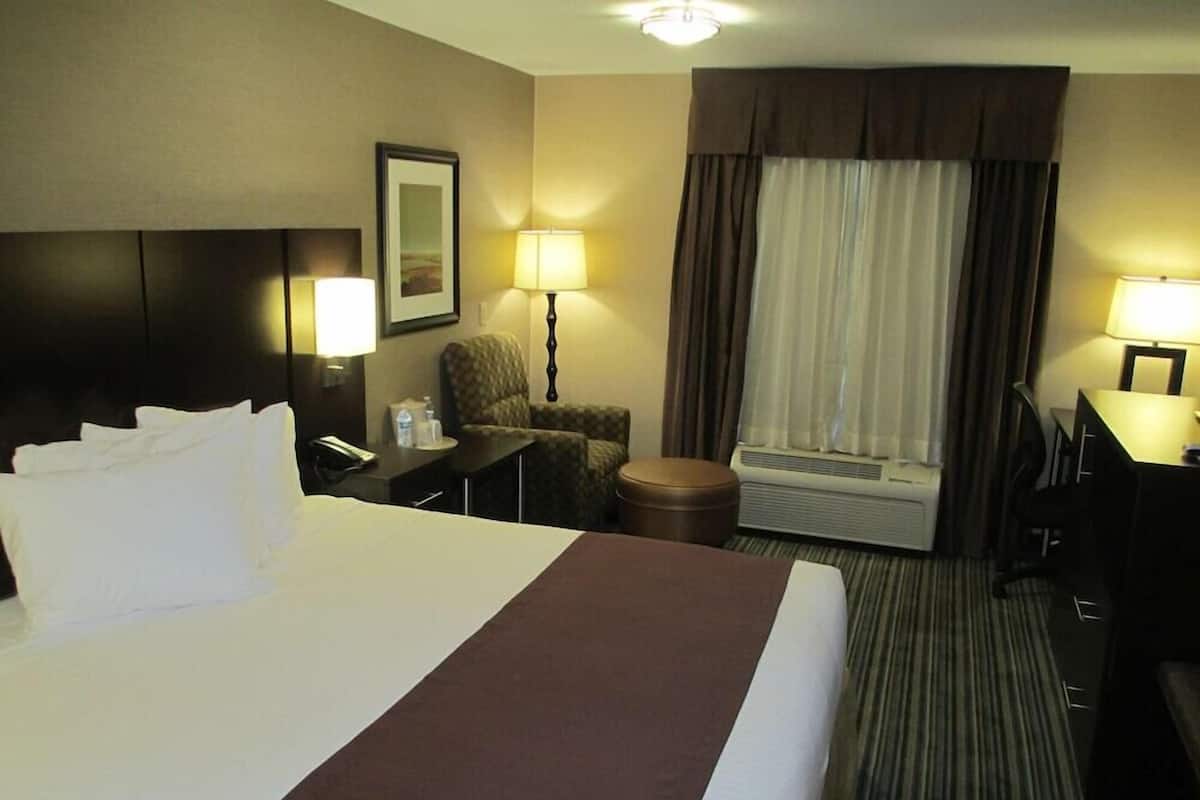 Ein Hotelzimmer mit einem großen Bett, einem Schreibtisch, einem Stuhl, einer Lampe und einer Klimaanlage.