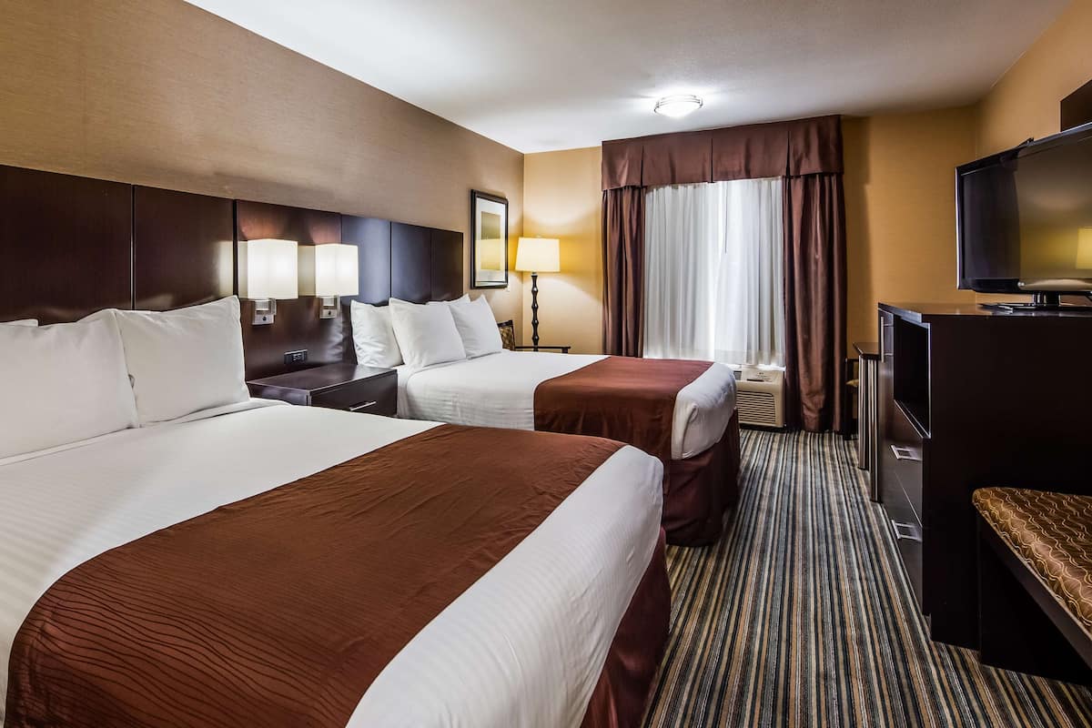 A hotel room with two beds, a TV, a desk, and a window with curtains.